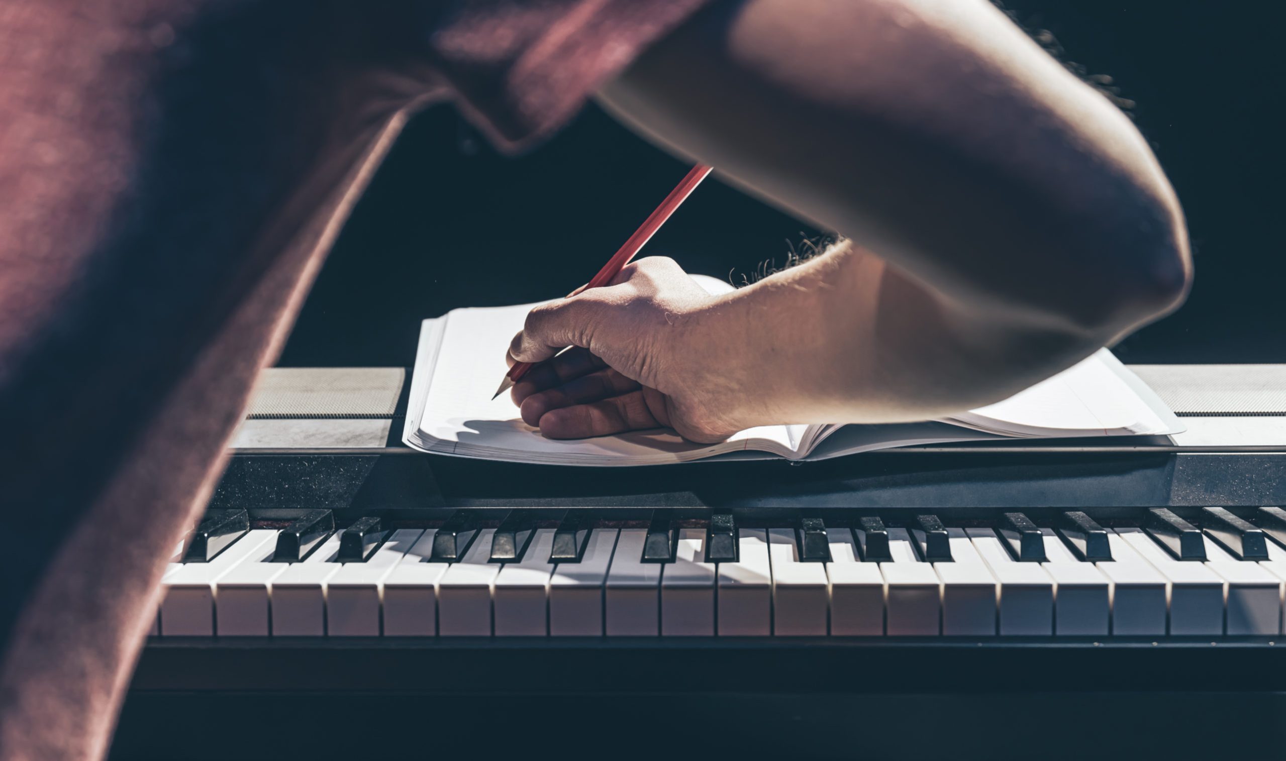 A man plays the piano and writes in a notebook in the dark.